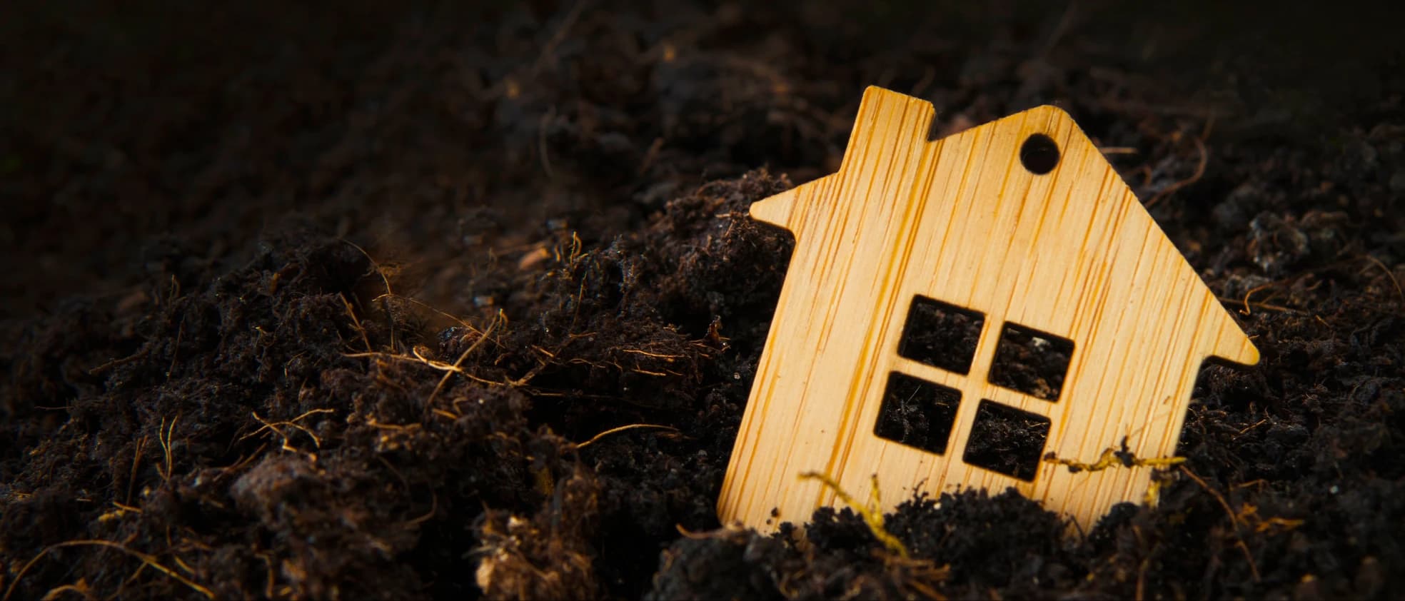 A small wooden house resting on dark soil — representing the foundations of a home.